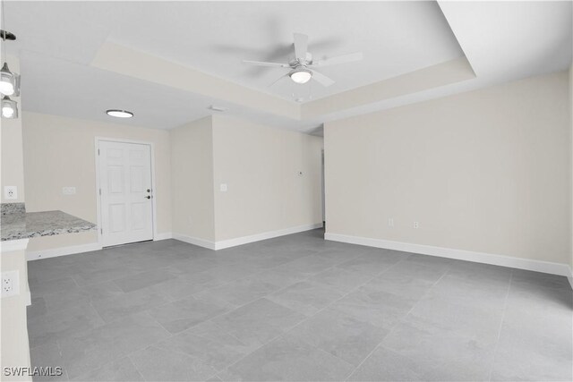 tiled spare room with a raised ceiling, ceiling fan, and baseboards