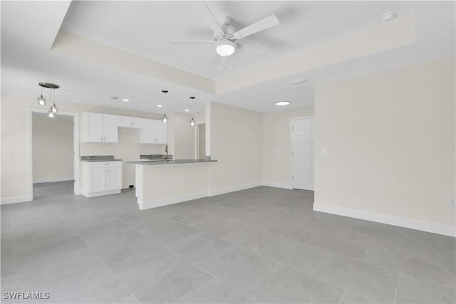 unfurnished living room featuring a tray ceiling, a ceiling fan, baseboards, and recessed lighting