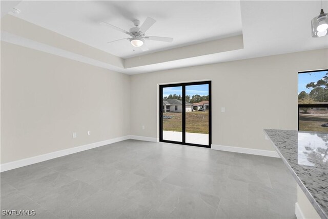 spare room with a tray ceiling, ceiling fan, and baseboards