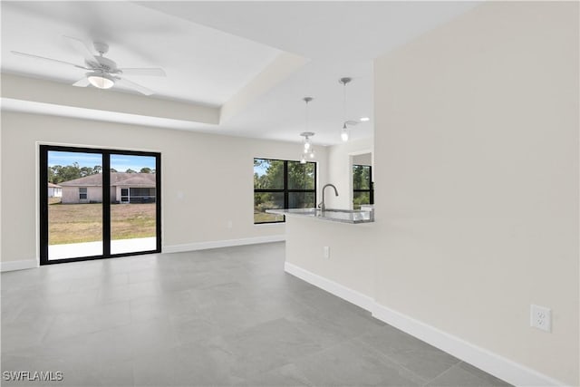 empty room featuring baseboards, ceiling fan, a sink, a raised ceiling, and recessed lighting