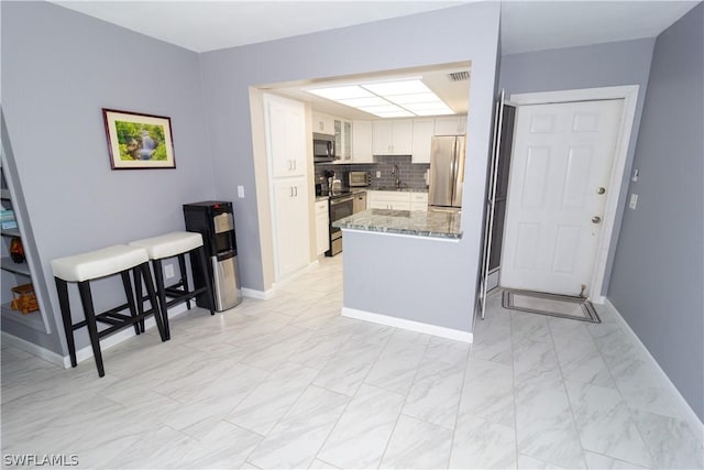 kitchen with stone counters, white cabinets, sink, kitchen peninsula, and stainless steel appliances