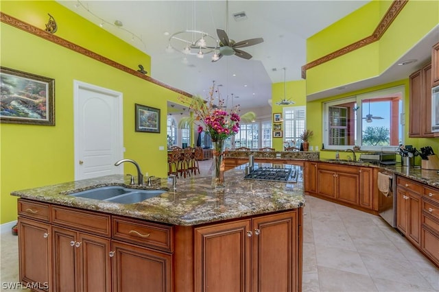 kitchen with dark stone countertops, a center island with sink, hanging light fixtures, and sink