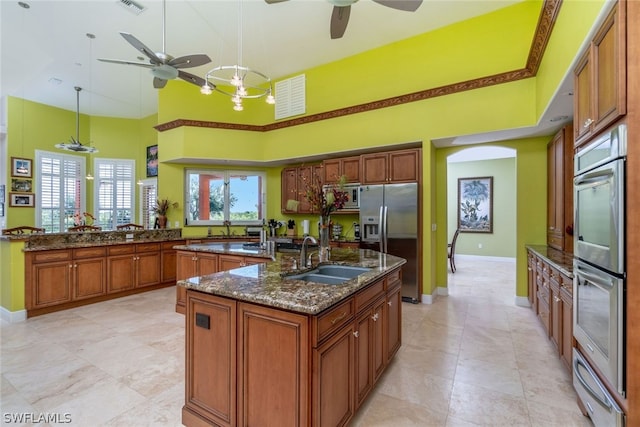 kitchen with stainless steel appliances, sink, a center island with sink, a high ceiling, and hanging light fixtures