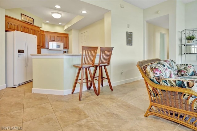 kitchen with white appliances, baseboards, brown cabinetry, a peninsula, and light countertops