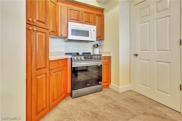 kitchen with light countertops, white microwave, brown cabinetry, and stainless steel range with electric stovetop