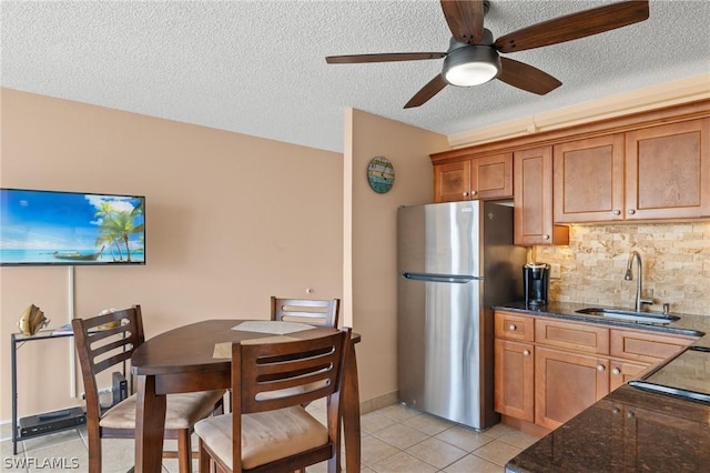 kitchen featuring stainless steel refrigerator, ceiling fan, sink, backsplash, and a textured ceiling