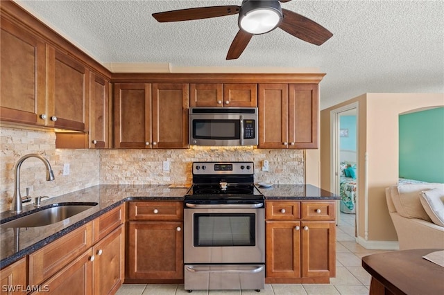 kitchen with appliances with stainless steel finishes, backsplash, dark stone countertops, and sink