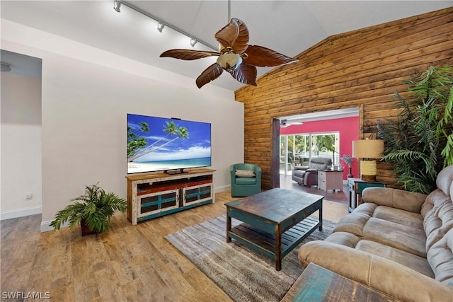 living room with ceiling fan, rail lighting, wood walls, wood-type flooring, and lofted ceiling