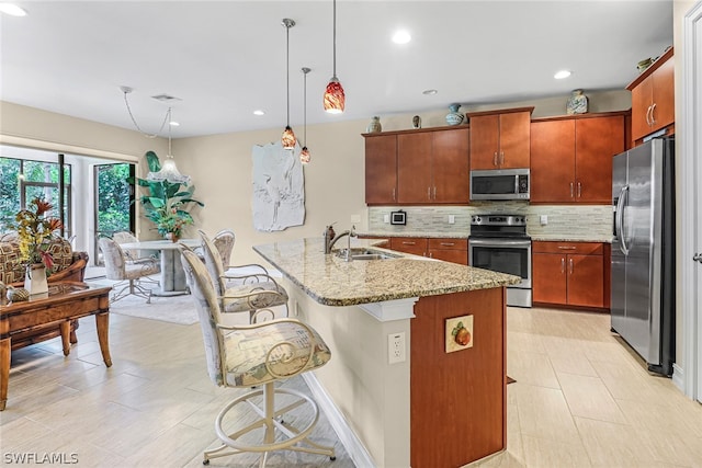 kitchen featuring pendant lighting, a kitchen bar, stainless steel appliances, sink, and light stone counters