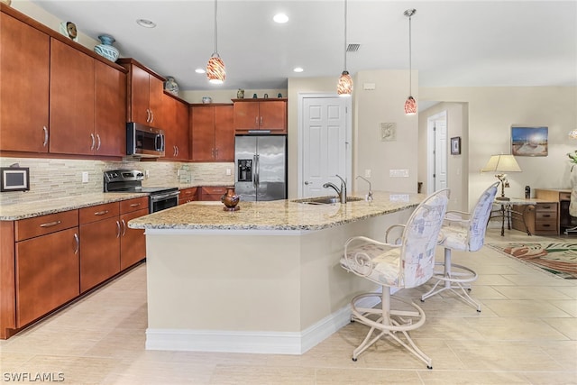 kitchen with pendant lighting, stainless steel appliances, decorative backsplash, sink, and a center island with sink