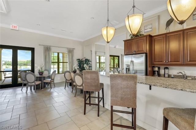 kitchen with decorative light fixtures, a kitchen breakfast bar, stainless steel fridge with ice dispenser, ornamental molding, and light stone counters