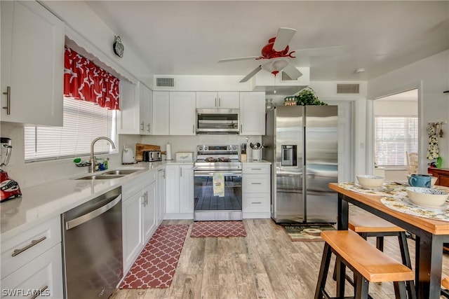 kitchen featuring ceiling fan, sink, stainless steel appliances, light hardwood / wood-style floors, and white cabinets