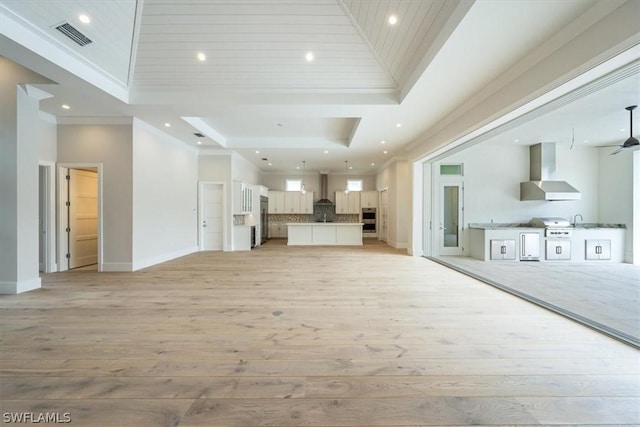 unfurnished living room with a tray ceiling, light hardwood / wood-style flooring, high vaulted ceiling, and sink