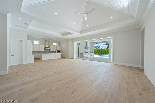 unfurnished living room featuring a tray ceiling, light hardwood / wood-style flooring, ceiling fan, and crown molding