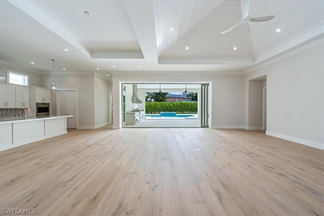 unfurnished living room with a tray ceiling, ceiling fan, ornamental molding, and light wood-type flooring