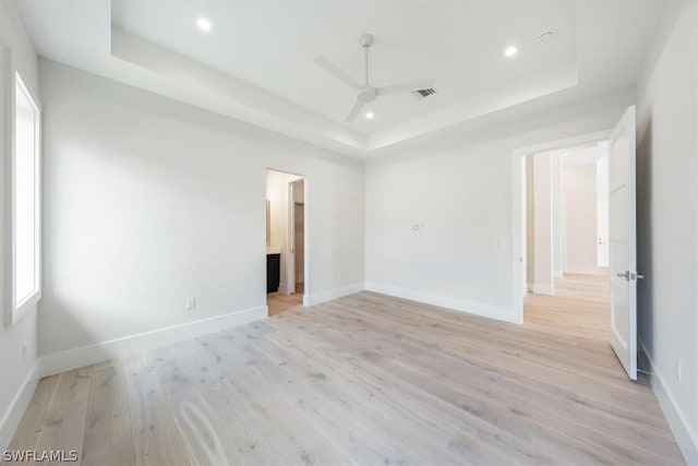 unfurnished room featuring light wood-type flooring, a tray ceiling, and ceiling fan