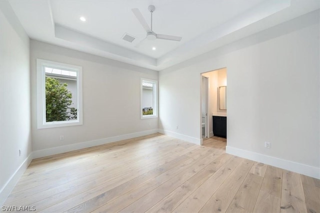 unfurnished bedroom with ceiling fan, light hardwood / wood-style floors, a tray ceiling, and ensuite bath