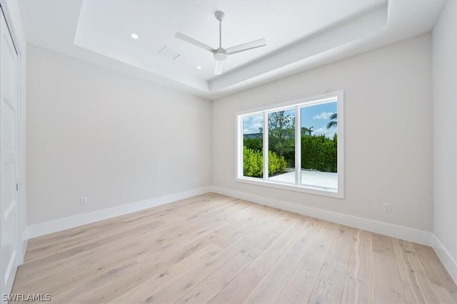 empty room featuring ceiling fan, light hardwood / wood-style floors, and a raised ceiling