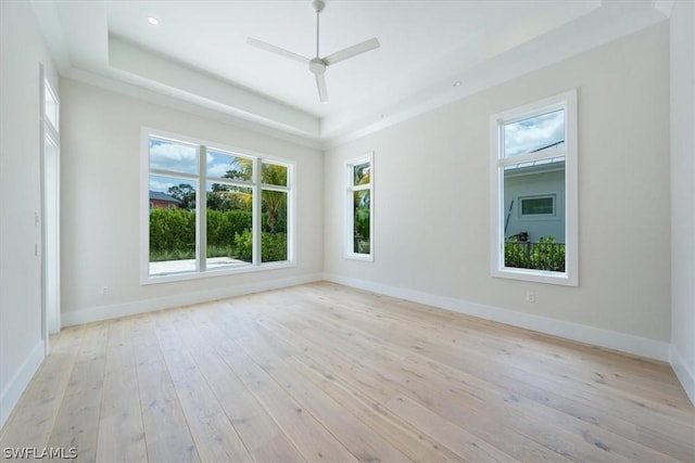 spare room with light wood-type flooring, a tray ceiling, and ceiling fan