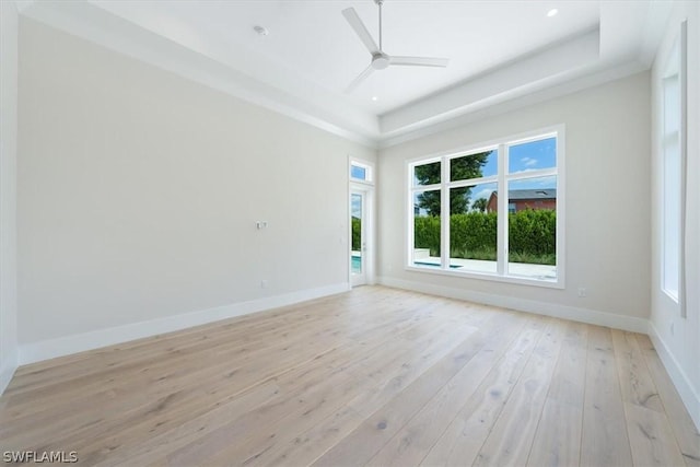 unfurnished room with ceiling fan, light wood-type flooring, and a tray ceiling