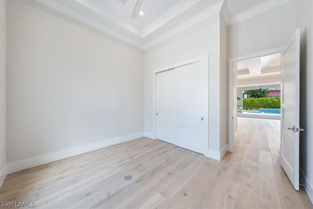 unfurnished bedroom with a raised ceiling, a closet, light hardwood / wood-style flooring, and ornamental molding