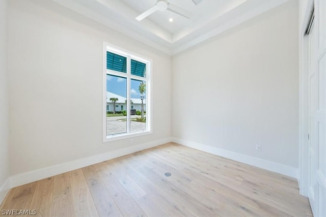 empty room with a raised ceiling, ceiling fan, and light hardwood / wood-style floors