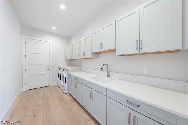 clothes washing area with washer and dryer, light hardwood / wood-style flooring, cabinets, and sink