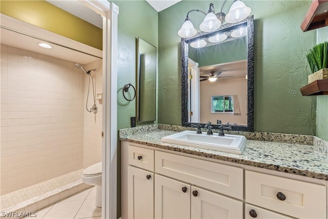 bathroom featuring tile patterned flooring, ceiling fan, a tile shower, toilet, and vanity