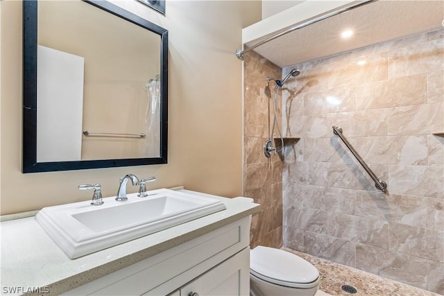 bathroom with toilet, a tile shower, and vanity