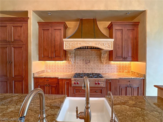 kitchen featuring premium range hood, backsplash, light stone countertops, and stainless steel gas stovetop