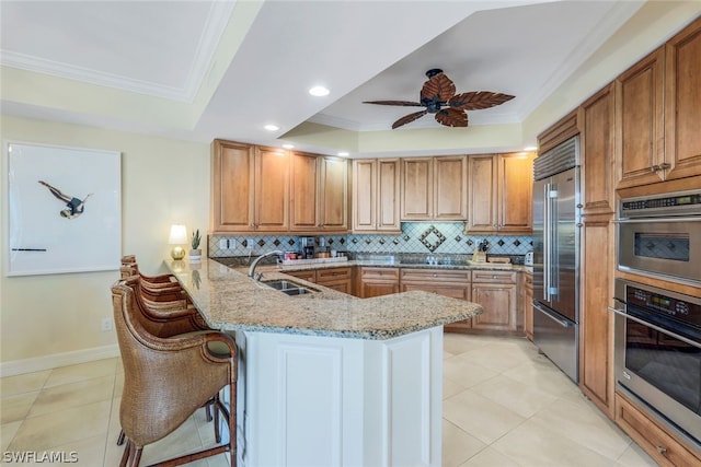 kitchen with kitchen peninsula, a kitchen breakfast bar, light stone counters, stainless steel appliances, and sink