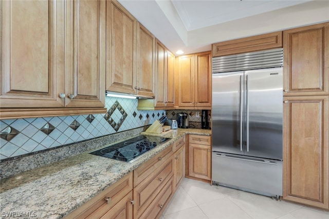 kitchen with light stone counters, built in refrigerator, black electric cooktop, decorative backsplash, and light tile patterned flooring