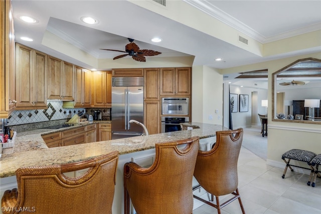 kitchen featuring kitchen peninsula, a kitchen bar, backsplash, light stone counters, and stainless steel built in fridge