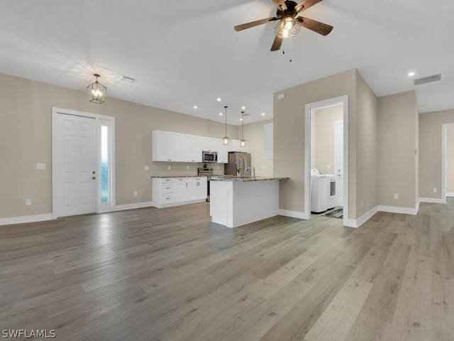 kitchen with stainless steel appliances, washing machine and dryer, decorative light fixtures, white cabinets, and light wood-type flooring