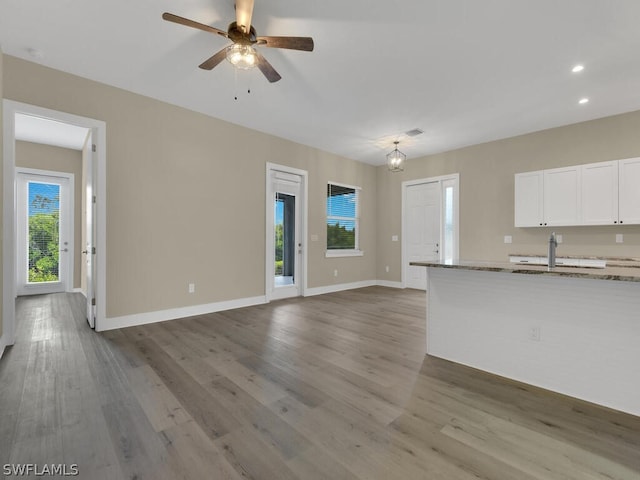 unfurnished living room with ceiling fan with notable chandelier, light wood-type flooring, and sink