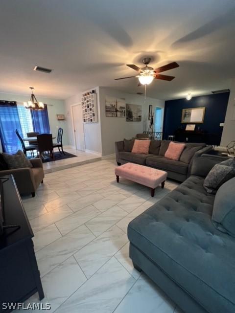 living room with visible vents, marble finish floor, ceiling fan with notable chandelier, and baseboards