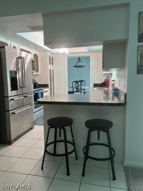 kitchen featuring light tile patterned floors, a breakfast bar, a peninsula, a sink, and appliances with stainless steel finishes