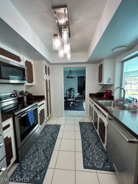 kitchen featuring light tile flooring, a tray ceiling, white cabinets, sink, and appliances with stainless steel finishes