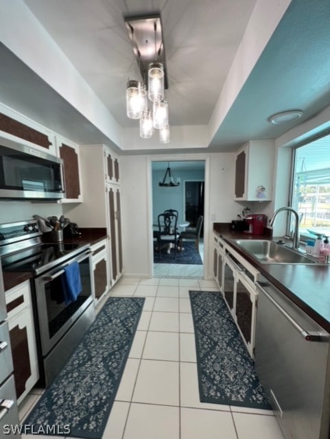 kitchen with a sink, a tray ceiling, dark countertops, appliances with stainless steel finishes, and light tile patterned floors