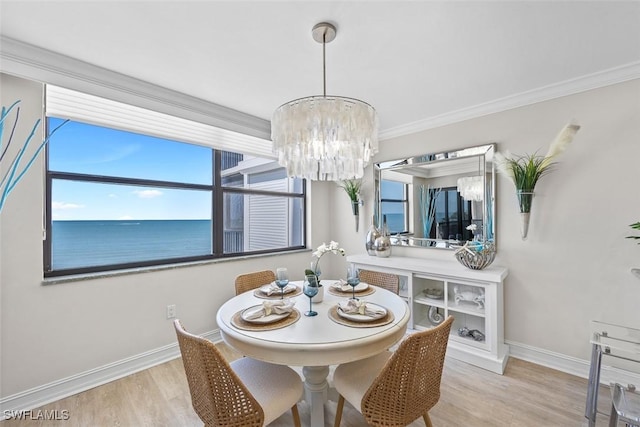 dining area with a water view, an inviting chandelier, light wood-type flooring, and ornamental molding