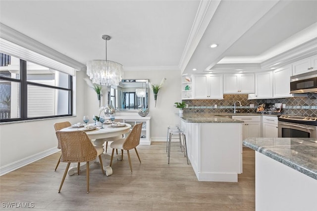 kitchen with stainless steel appliances, white cabinets, pendant lighting, ornamental molding, and dark stone countertops