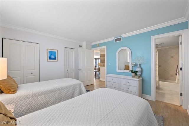 bedroom featuring light wood-type flooring, ornamental molding, connected bathroom, and multiple closets