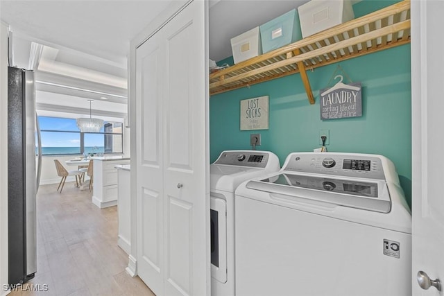 clothes washing area featuring light hardwood / wood-style flooring, an inviting chandelier, and washer and clothes dryer