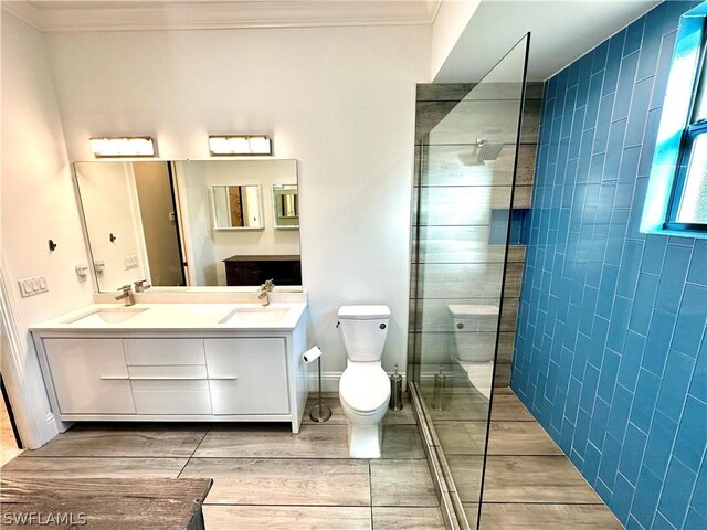 bathroom featuring vanity, toilet, a tile shower, and crown molding