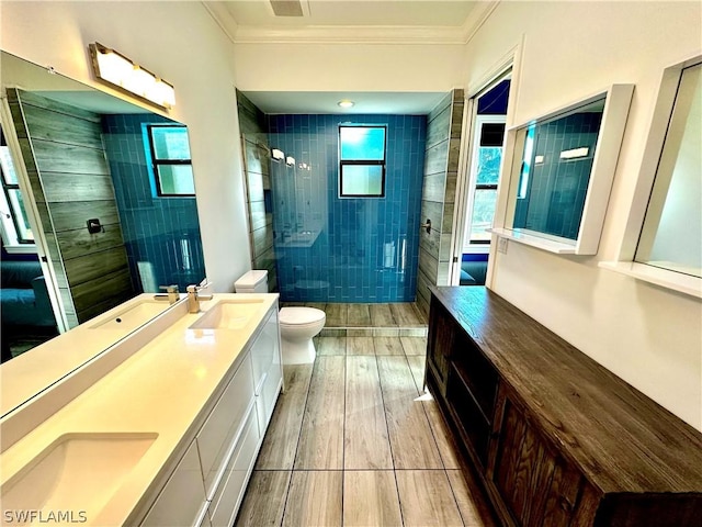 bathroom featuring vanity, toilet, ornamental molding, and a tile shower