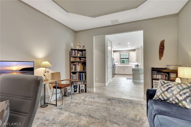 living room with light wood-type flooring, a raised ceiling, and sink