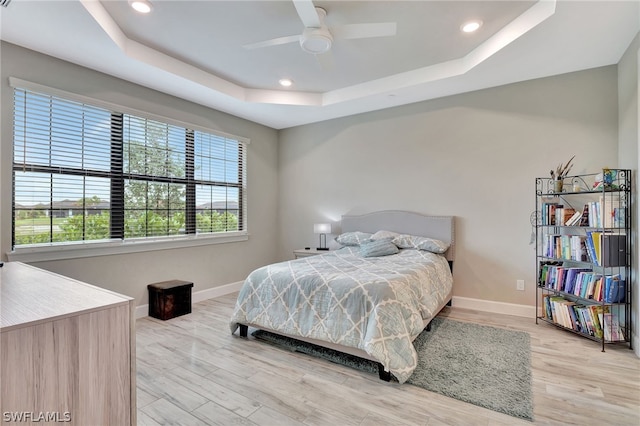 bedroom with a tray ceiling, ceiling fan, and light hardwood / wood-style flooring