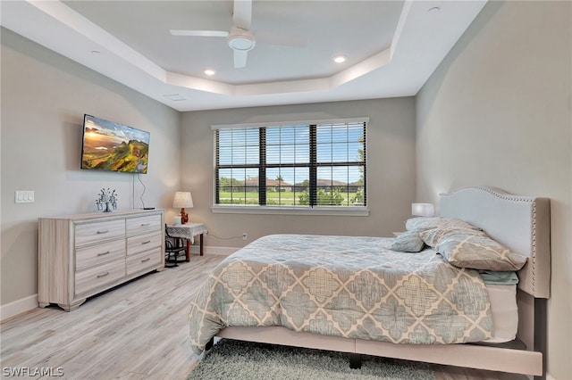 bedroom featuring light wood-type flooring, a raised ceiling, and ceiling fan