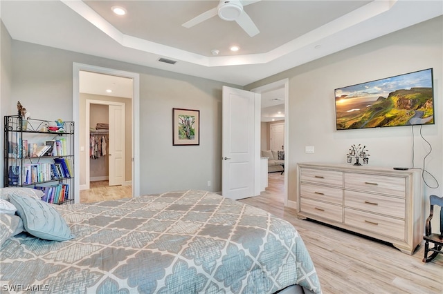 bedroom featuring ceiling fan, a tray ceiling, and light hardwood / wood-style flooring