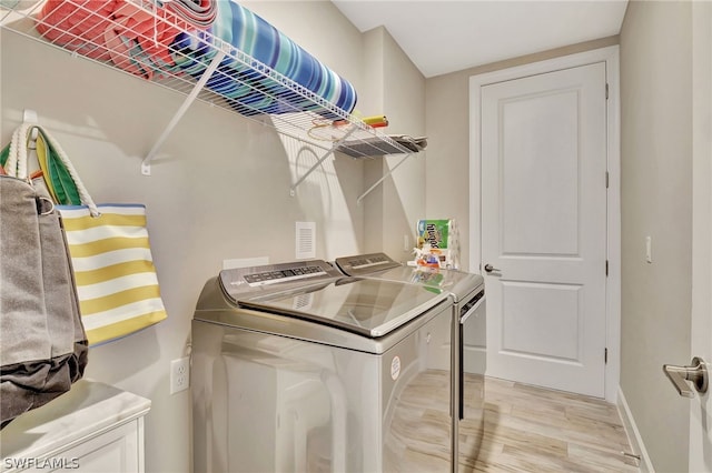 clothes washing area featuring washing machine and clothes dryer and light hardwood / wood-style flooring